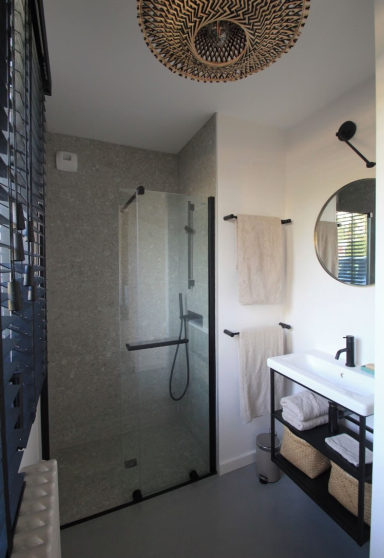 Salle de bains moderne avec douche vitrée, miroir rond et lavabo sur meuble.