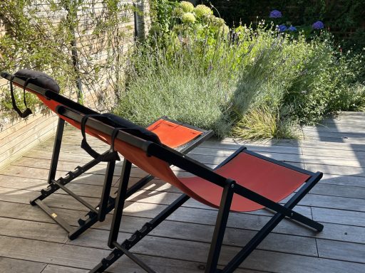 Chaises longues orange en métal sur une terrasse, entourées de plantes vertes.