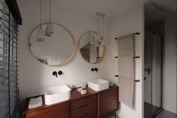 Salle de bain moderne avec deux lavabos, miroirs ronds et serviettes suspendues.