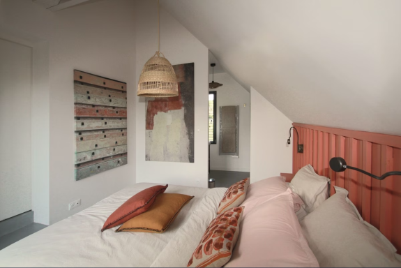 Chambre moderne avec lit orange, coussins décoratifs et éclairage suspendu.