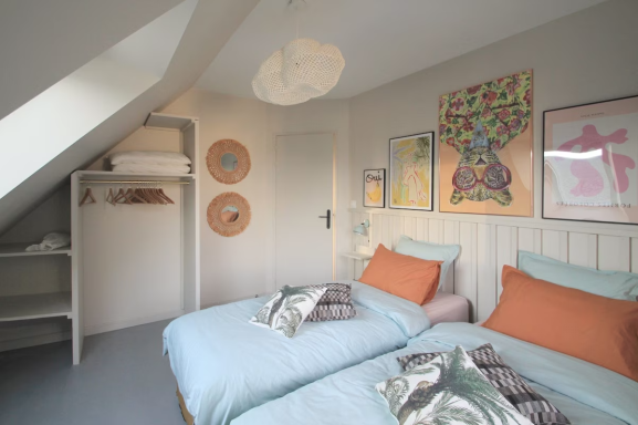 Chambre moderne avec deux lits jumeaux, décor pastel et tableaux artistiques aux murs.