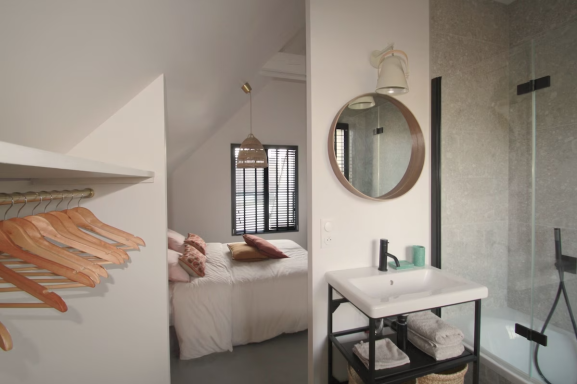 Chambre moderne avec salle de bain, miroir rond et rangements minimalistes.