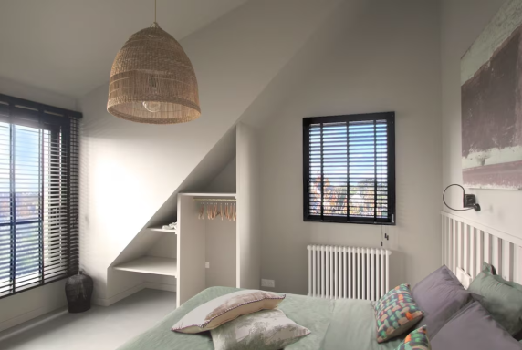 Chambre lumineuse avec fenêtres, lit confortable et décoration minimaliste.