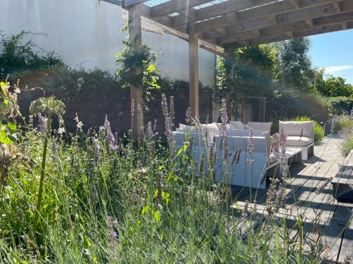 Terrasse lumineuse avec des bancs blancs et des plantes fleuries environnantes.